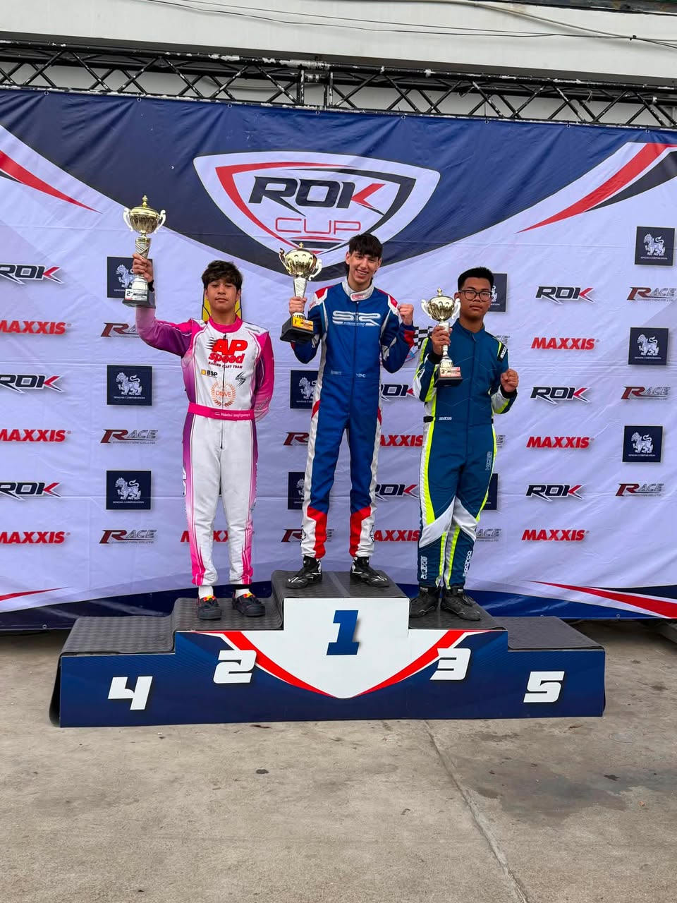 Three kart drivers holding trophies on a ROK Cup podium, with Yehonatan Moshe standing in first place